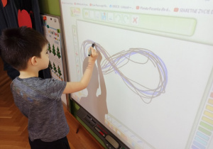 Chłopiec rysuje na tablicy multimedialnej.
